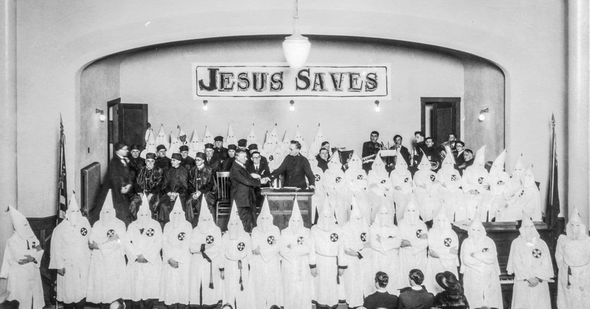 Ku Klux Klan in a church sanctuary with a banner in the background that reads Jesus Saves